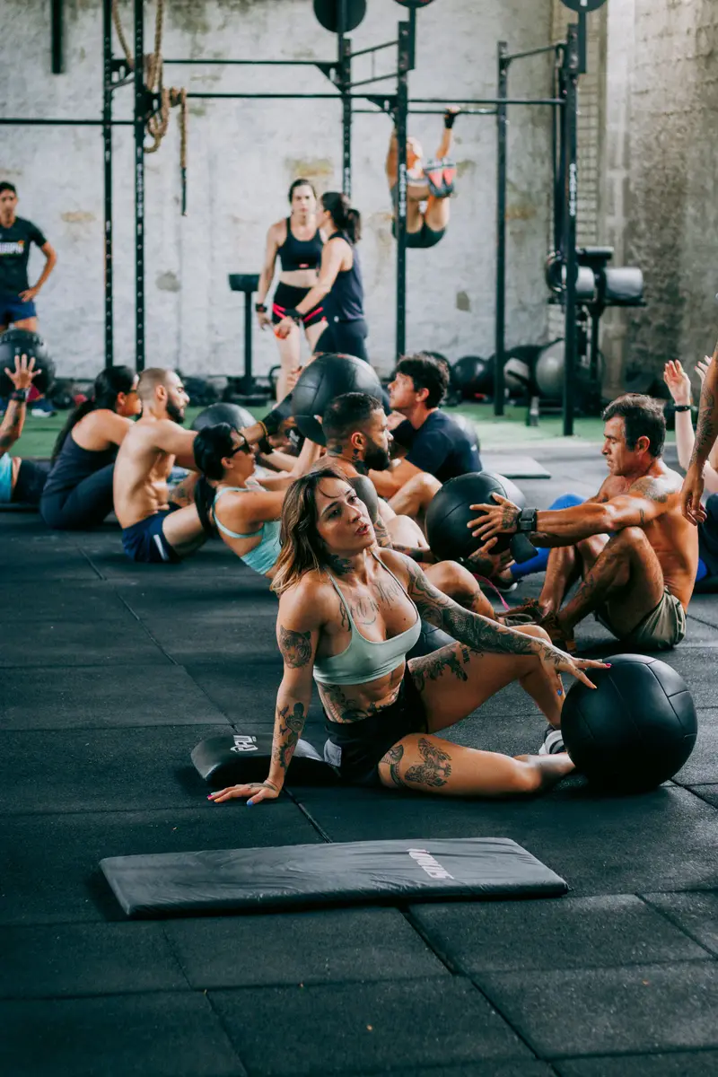 A group doing medicine-ball sit-ups on rubber flooring in a gym with pull-up rigs