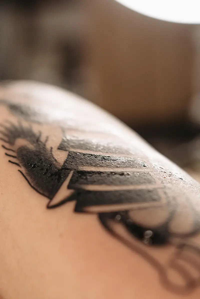 Freshly finished black wing tattoo with soft shading on a shoulder