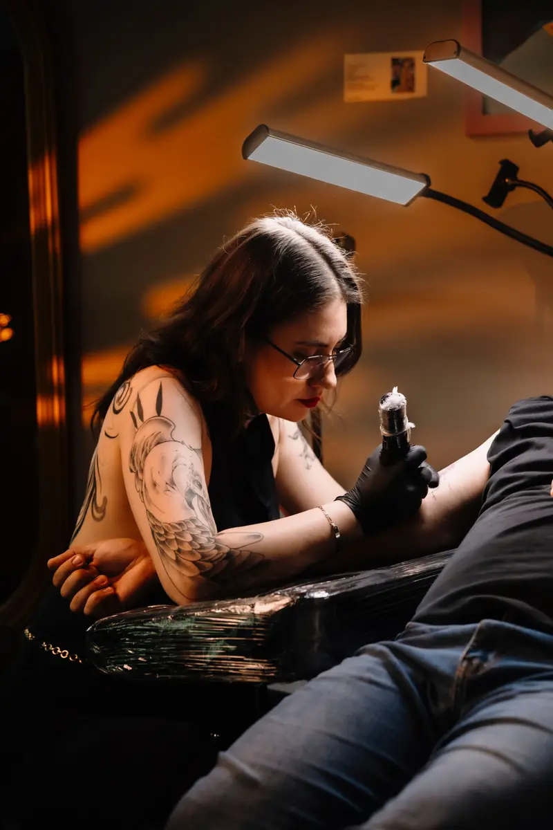Tattoo artist working on a client's arm under a low lamp